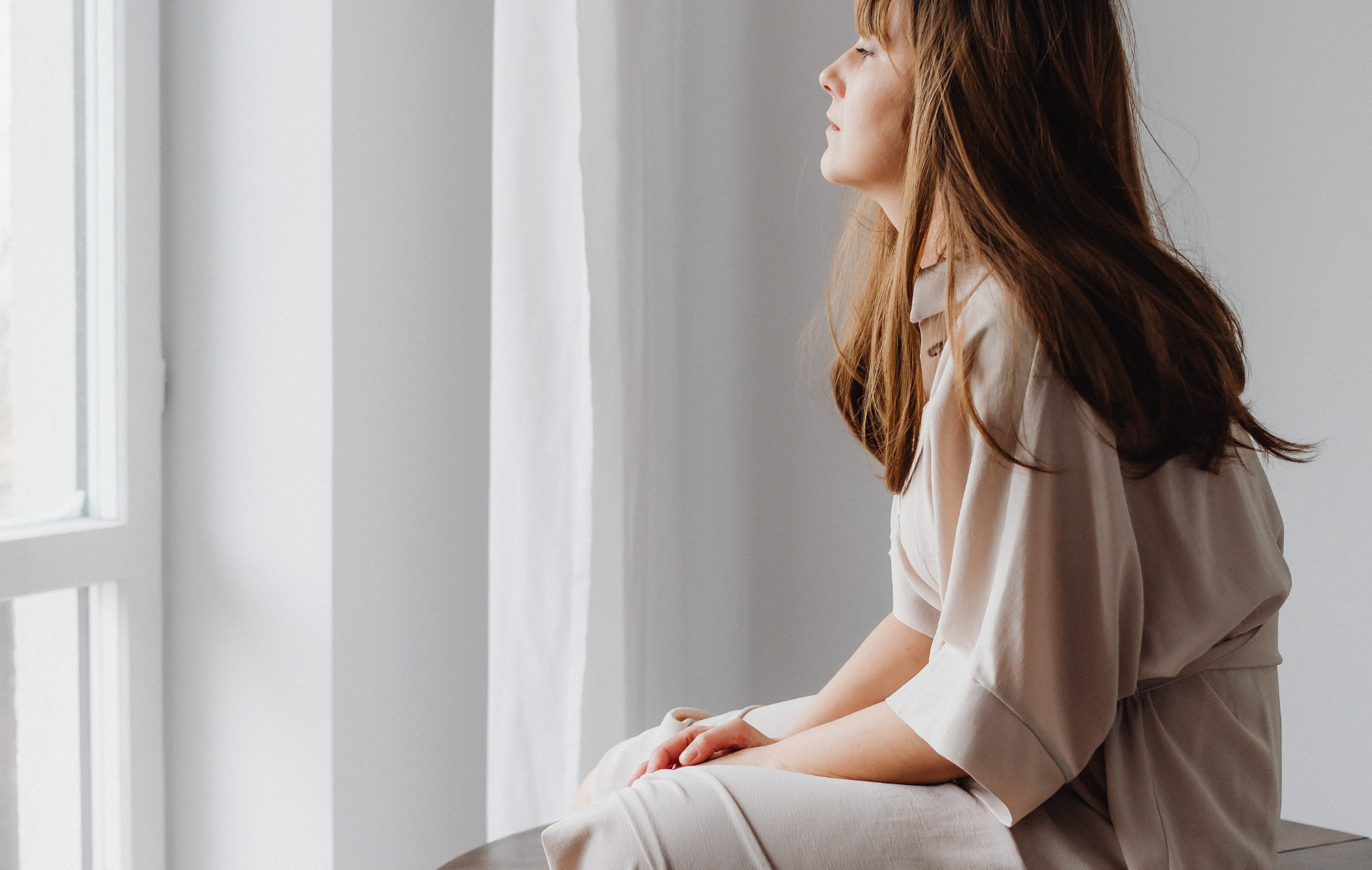 Personne assise près d'une fenêtre, la main posée sur le cœur, dans un moment de calme et de bienveillance envers soi